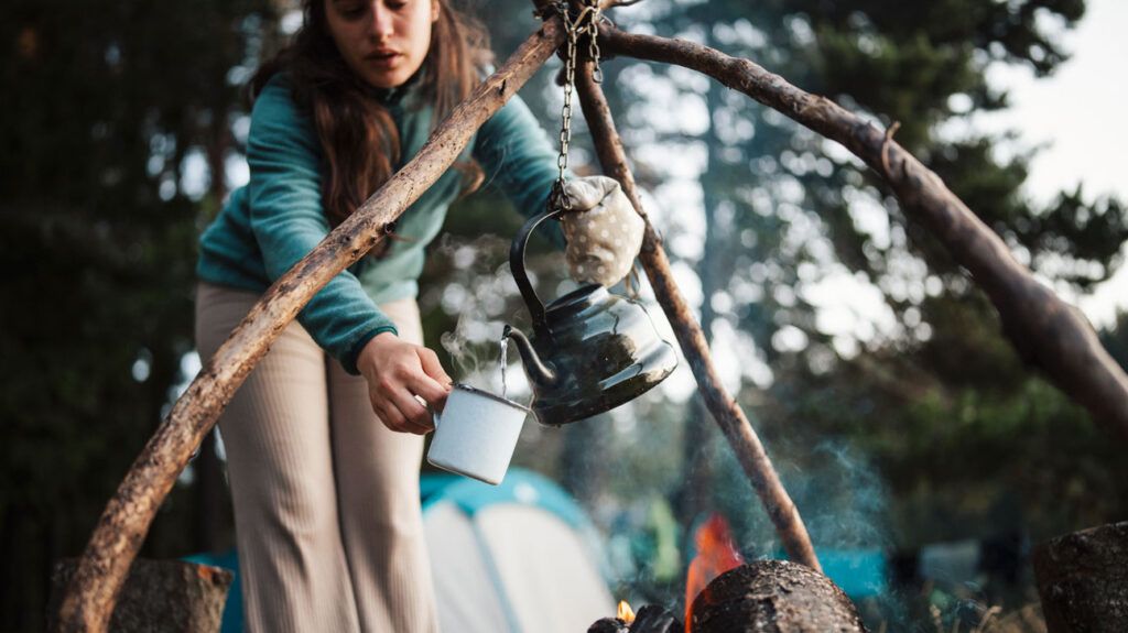 A person pouring a pot of coffee over an outdoor fire, a common source of burns.