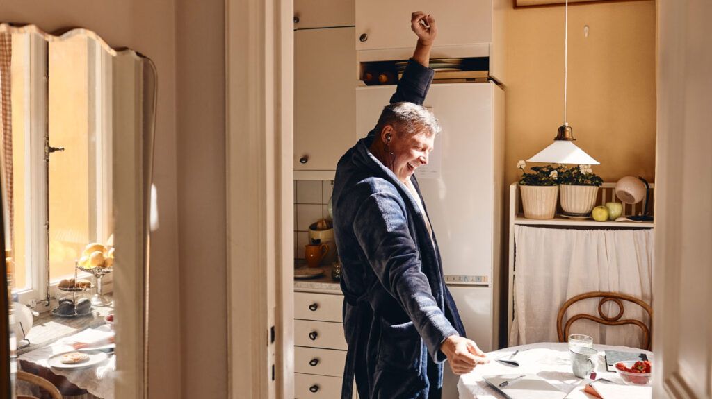 A man standing in the kitchen with headphones on and one arm up in the air. He is smiling and having fun, enjoying reduced pain due to diclofenac.