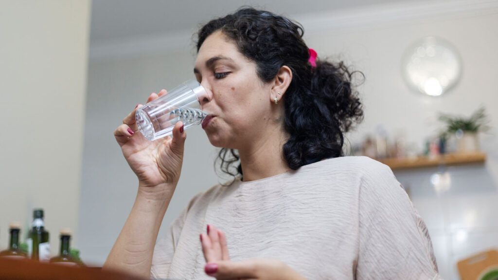 A woman taking a pill with a glass of water.