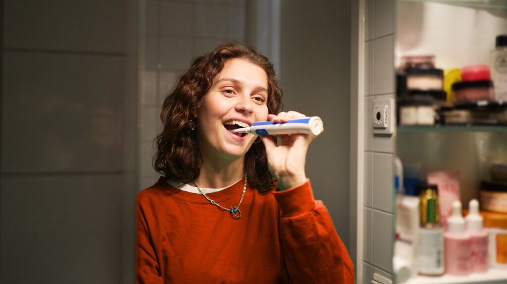 A person brushing their teeth, smiling, to get rid of gingivitis.