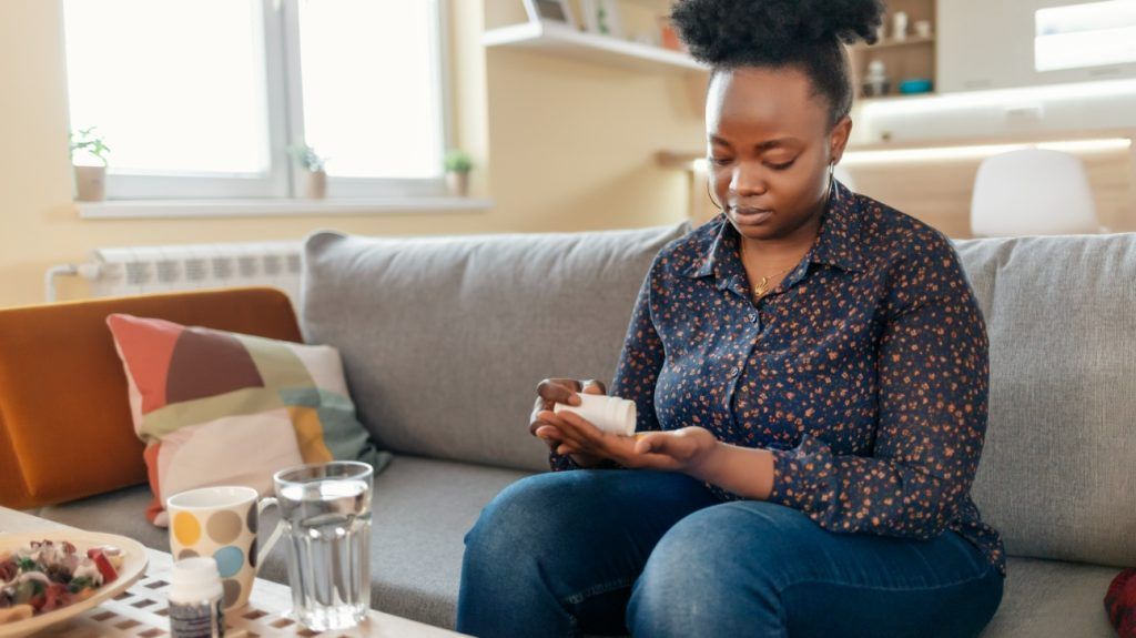 A person sitting on a sofa, pouring pills into their hand from a bottle.