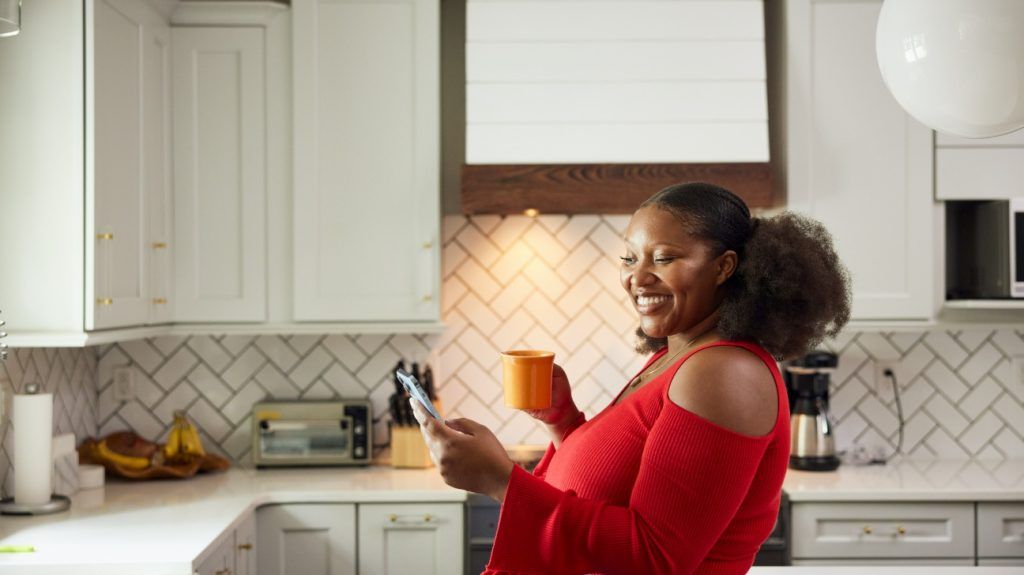 A plus-size woman in her kitchen researching on her phone.