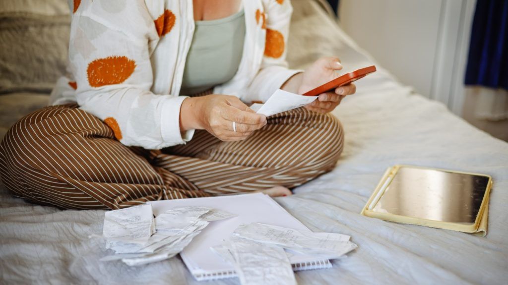 A person sitting on a bed budgeting with receipts.