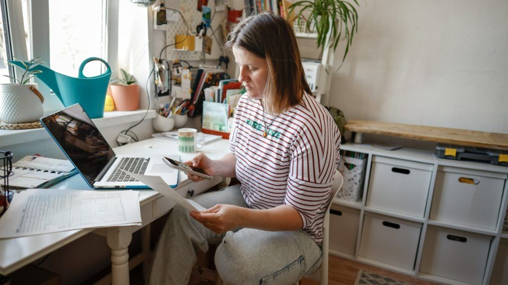 A person researching their insurance policy with a phone, laptop, and documents.
