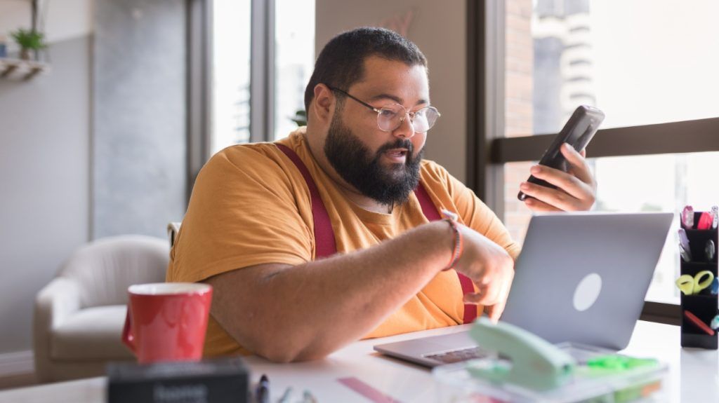 A man researching on his laptop and phone about buying medications online.