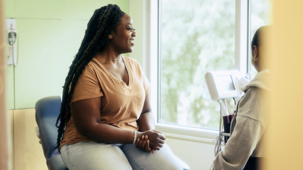 A plus-size woman speaking with a healthcare professional in an exam room.